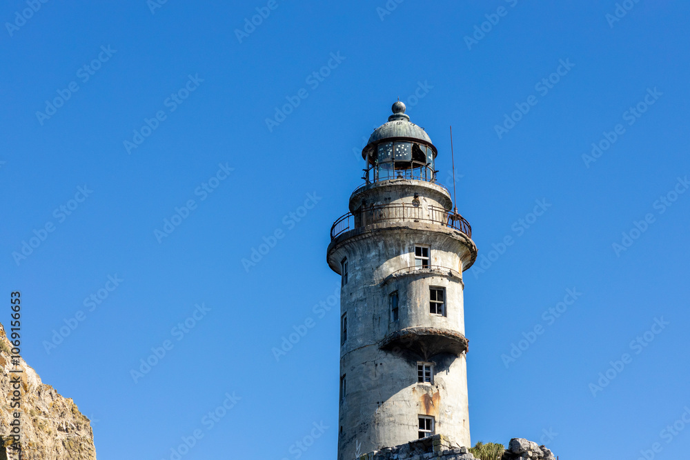 Aniva - The abandoned lighthouse in the Sakhalin Island, Korsakov district, Russia. Pacific ocean. The abandoned lighthouse Island Blue sea. Beautiful view. Blue sky and blue Pacific ocean. Aniva - The abandoned lighthouse in the Sakhalin Island, Korsakov district, Russia. Pacific ocean. The abandoned lighthouse Island Blue sea. Beautiful view. Blue sky and blue Pacific ocean.