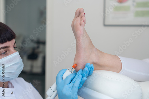 The podologist treats the feet using electric device machine. Patient on medical pedicure procedure, visiting podiatrist. Peeling feet. Foot treatment in SPA salon.Podiatry clinic photo