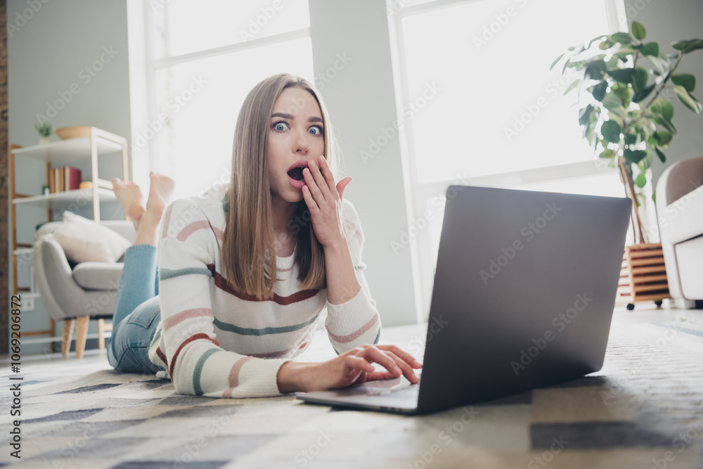 Surprised young woman at home reacts to unexpected news on laptop in cozy living room using natural daylight Surprised young woman at home reacts to unexpected news on laptop in cozy living room using natural daylight