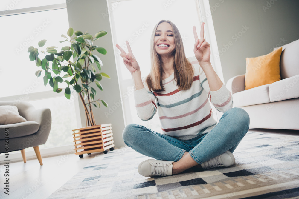 Young woman with a happy expression showing peace signs in a bright living room interior, enjoying comfortable leisure time at home. Young woman with a happy expression showing peace signs in a bright living room interior, enjoying comfortable leisure time at home.