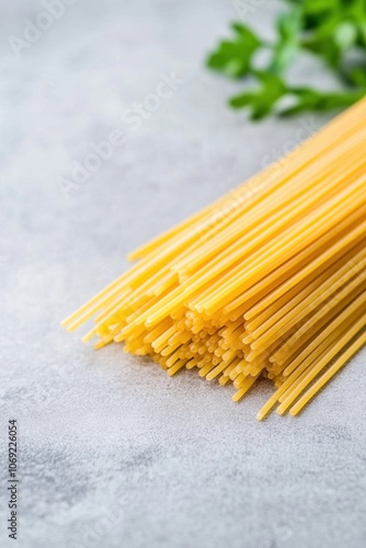 Close-up of uncooked yellow spaghetti noodles on a gray background with a blurred green leaf in the background