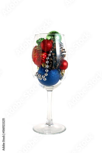 A glass goblet filled with Christmas balls stands on a white background.