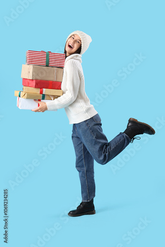 Happy young woman with Christmas gifts on blue background