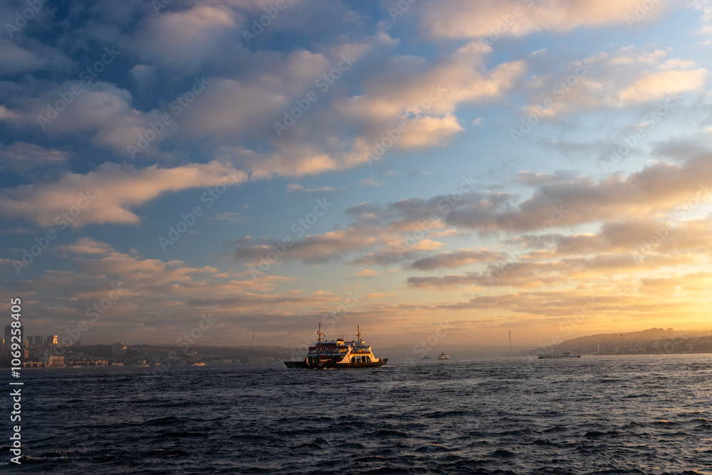 An amazing sunrise over the Bosphorus. Silhouette of a ferry in the vibrant sky, sailing on calm waters. The sky is ablaze with a kaleidoscope of colors, from deep blue to bright orange and yellow. An amazing sunrise over the Bosphorus. Silhouette of a ferry in the vibrant sky, sailing on calm waters. The sky is ablaze with a kaleidoscope of colors, from deep blue to bright orange and yellow.