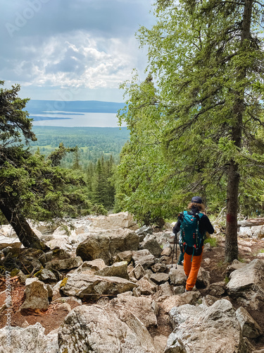 A person carrying a mediumsized backpack strolls along a rocky path in a tranquil woodland, taking in the stunning beauty of nature and the soothing sounds of wildlife all around them photo