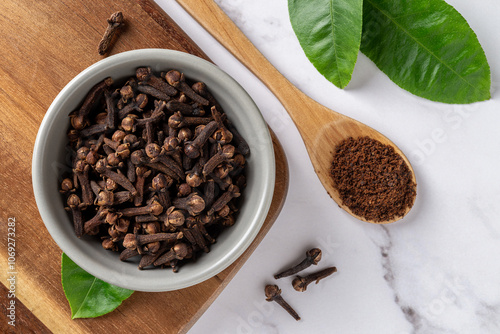 Cloves spice whole and ground over marble background. Dry clove buds in a gray ceramic bowl and spoon of powdered spice. Macro. Concept of spice and condiment.