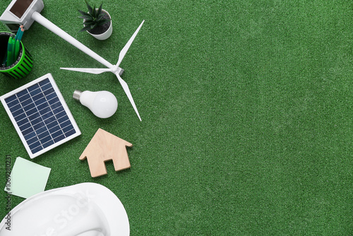 Wind turbine with solar panel, light bulb, house figure and hardhat on grass. Green Energy concept photo