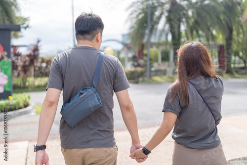 A Chinese-Malaysian couple in their 30s walk together in a green park with abundant water in Kuala Lumpur, Malaysia, on a sunny day in June 2024.