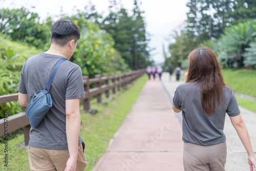 A Chinese-Malaysian couple in their 30s walk together in a green park with abundant water in Kuala Lumpur, Malaysia, on a sunny day in June 2024.