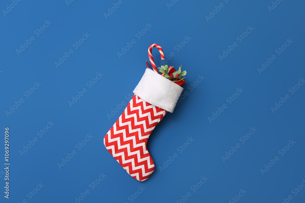 Obraz premium Christmas sock with gift, mistletoe twig and candy cane hanging on blue wall