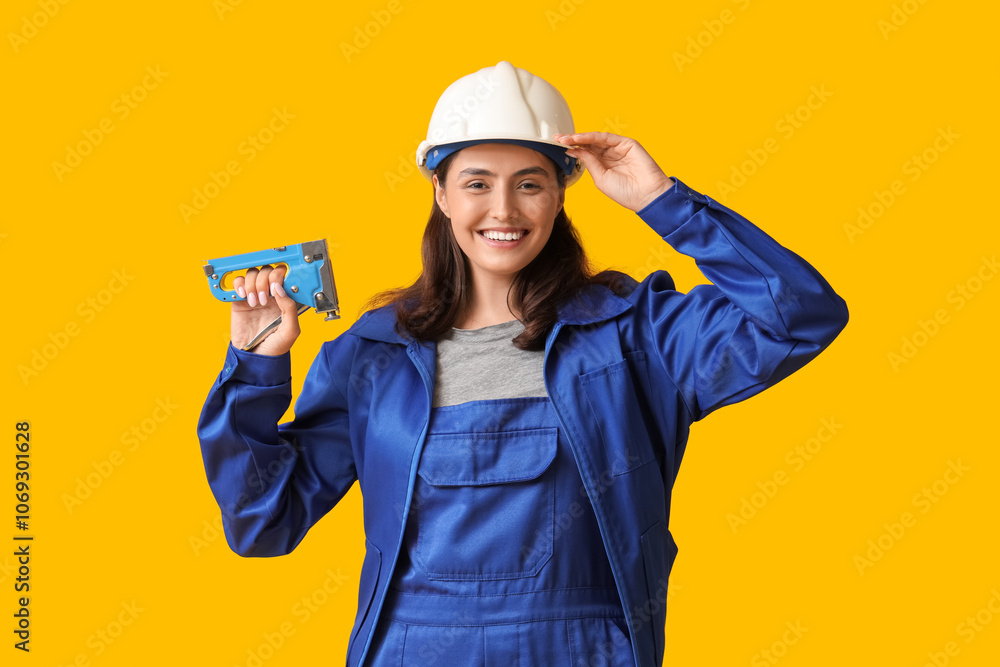 Young female construction worker with industrial stapler on yellow background. Woman in male profession concept