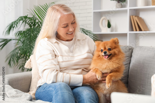 Happy senior woman with cute Pomeranian dog sitting on sofa at home