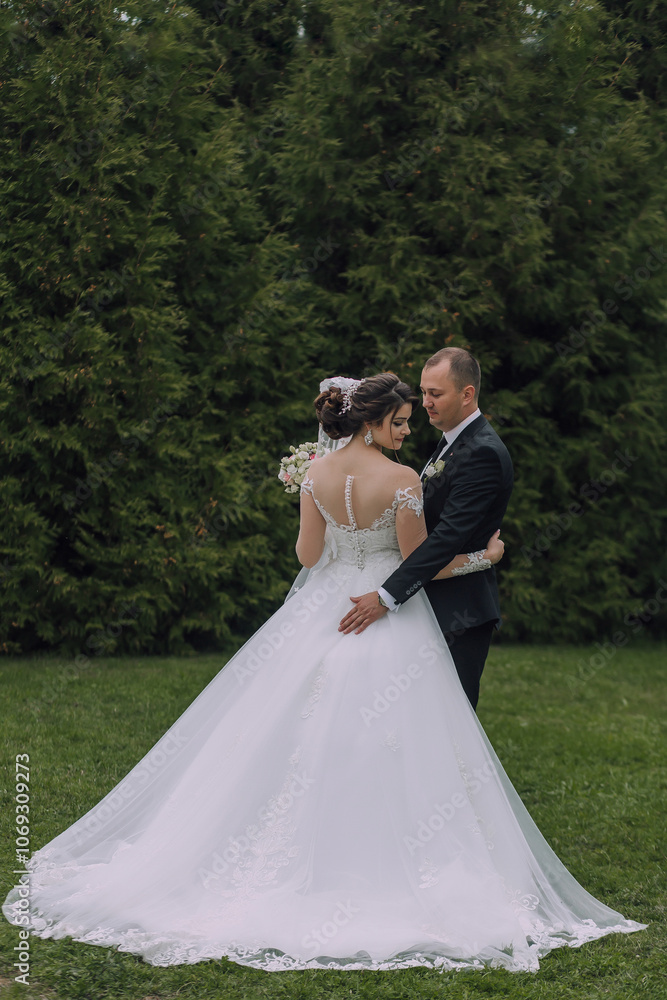 A bride and groom are standing in a grassy field, with the bride wearing a white dress and the groom wearing a black suit A bride and groom are standing in a grassy field, with the bride wearing a white dress and the groom wearing a black suit
