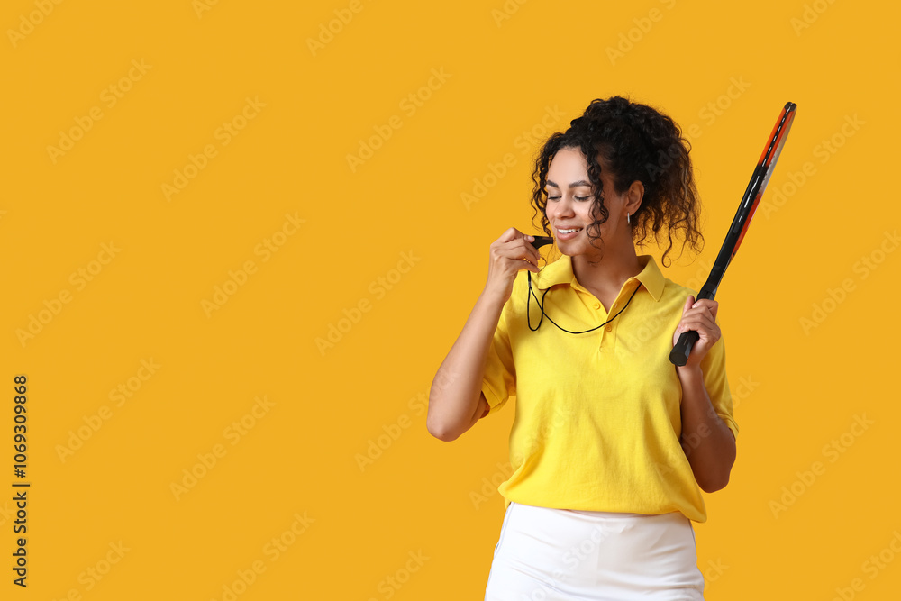 Female African-American tennis trainer with racket blowing in whistle on yellow background Female African-American tennis trainer with racket blowing in whistle on yellow background
