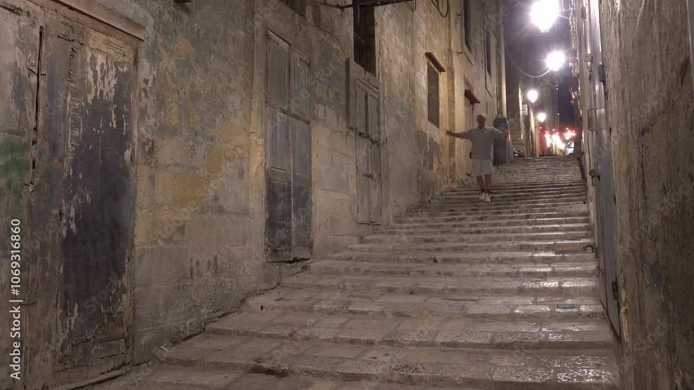 Valletta, Malta A male tourist walks on ancient steps in Old Valletta at night on North Street. Valletta, Malta A male tourist walks on ancient steps in Old Valletta at night on North Street.