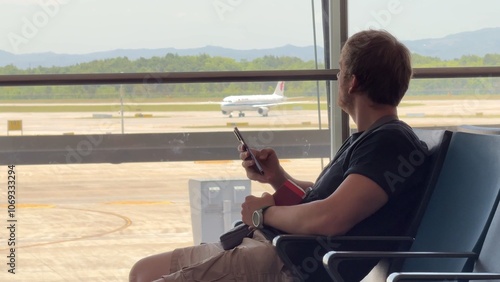Wallpaper Mural man at the airport with an airplane in the background waiting for a flight, using a phone, looking out the window and at his watch Torontodigital.ca