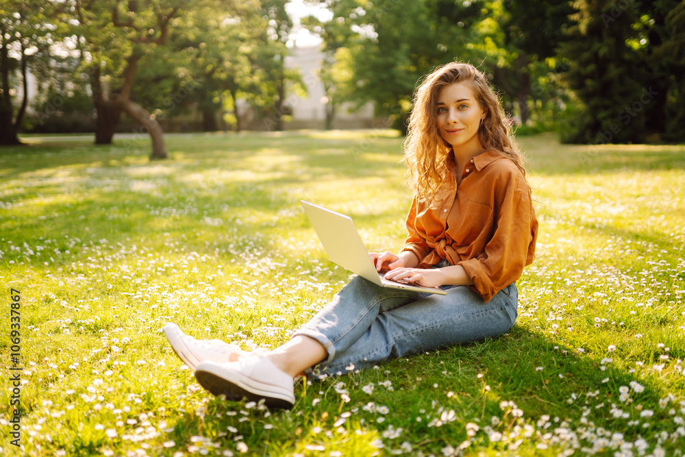 Young Woman sitting on grass ground, working on laptop. Online education, Freelance work, technology concept. Mobile Office. Young Woman sitting on grass ground, working on laptop. Online education, Freelance work, technology concept. Mobile Office.