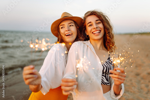 Beautiful Two women holding sparkler celebration on beach. They are having a great time together! Summer holidays, party, vacation, relax. #1069355496