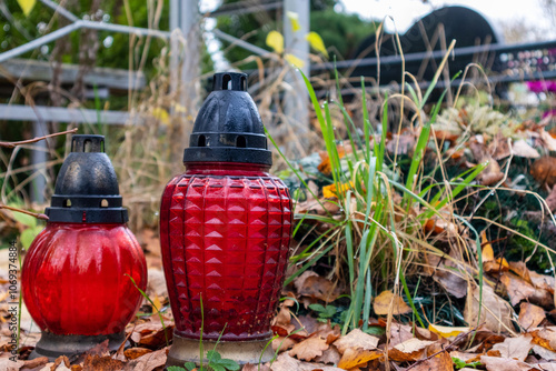 Red memorial lanterns placed among fallen leaves at a cemetery