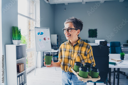 Photo of lovely pensioner lady hold papers cups drinking coffee wear plaid yellow shirt coworking successful nice light office photo