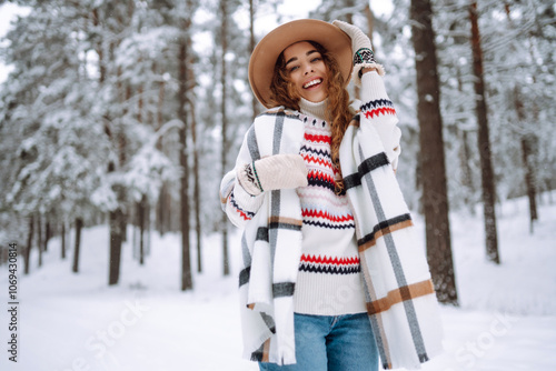 Smiling young woman enjoys winter weather at snowy winter park. Boho style. Holidays, rest, travel concept.