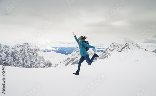 a woman in a blue jacket jumps against the backdrop of snow-capped mountains, winter in the mountains