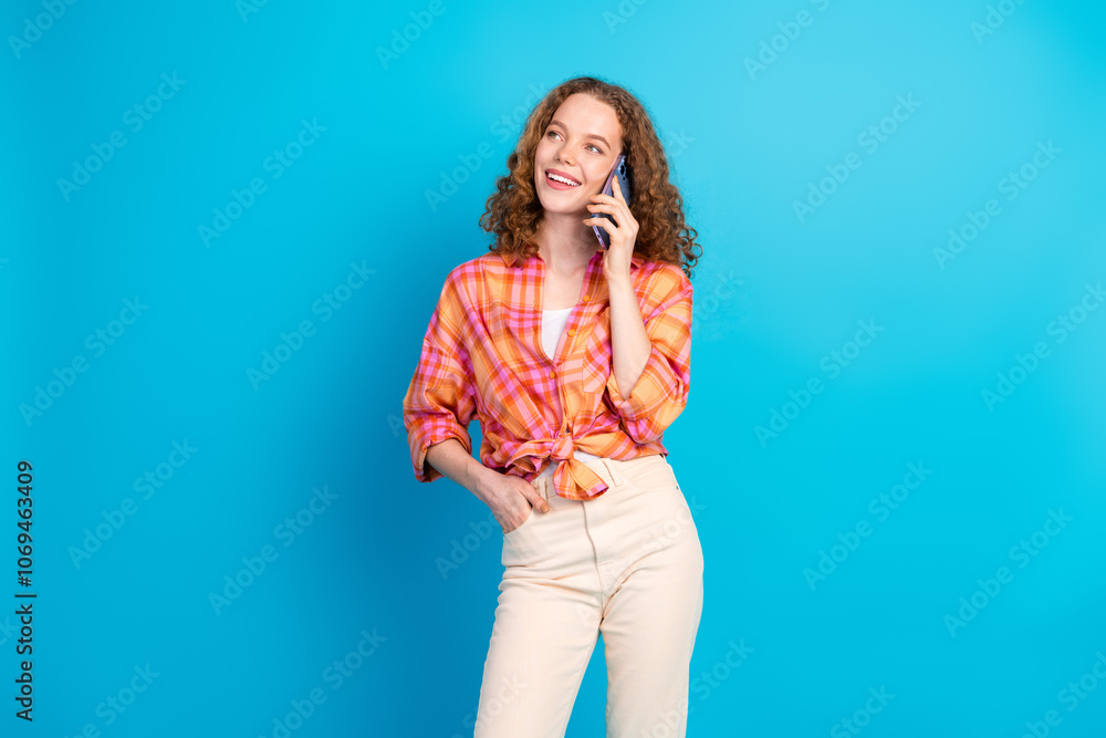 Young redhaired woman in casual outfit talks on phone against a vibrant blue background, expressing happiness and joy. Young redhaired woman in casual outfit talks on phone against a vibrant blue background, expressing happiness and joy.