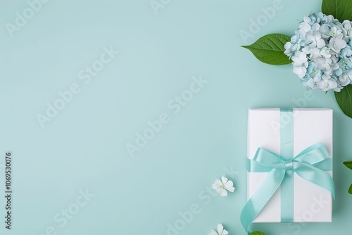 White gift box with blue ribbon, hydrangea flowers on light turquoise background, elegant celebration design, decorative floral flat lay, minimal and creative composition

