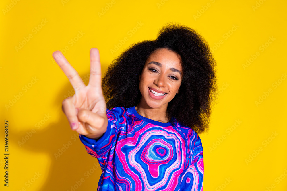 Photo portrait of attractive young woman show v-sign dressed stylish colorful blue clothes isolated on yellow color background Photo portrait of attractive young woman show v-sign dressed stylish colorful blue clothes isolated on yellow color background