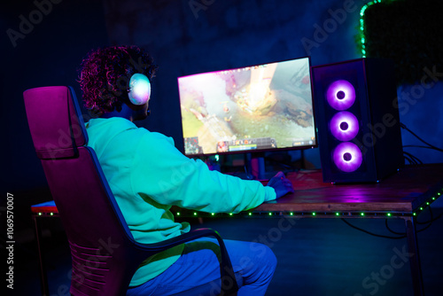 Photo of cute young guy bck view play gamer computer purple blue neon light indoors late night photo