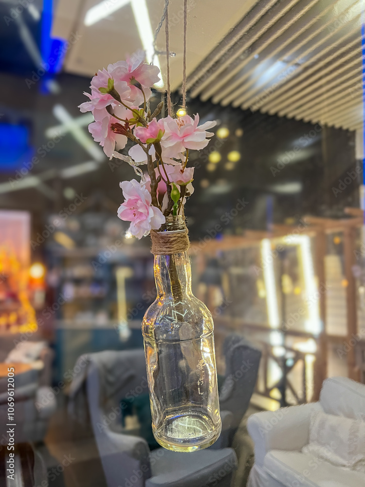 Fototapeta premium Vintage glass bottle with bouquet of cherry blossoms in a glass vase in a cafe hanging in the air