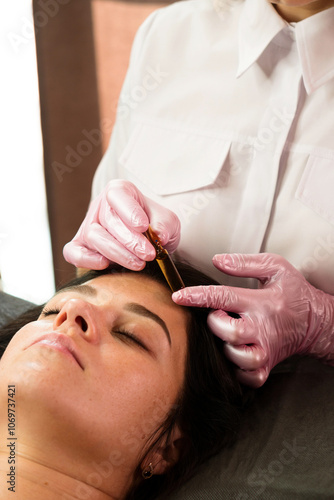 Beautician applies serum from ampoule to client’s forehead