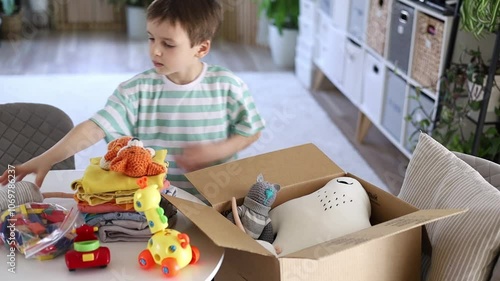 Caucasian preschool boy collects his toys in a cardboard box on the sofa in the living room