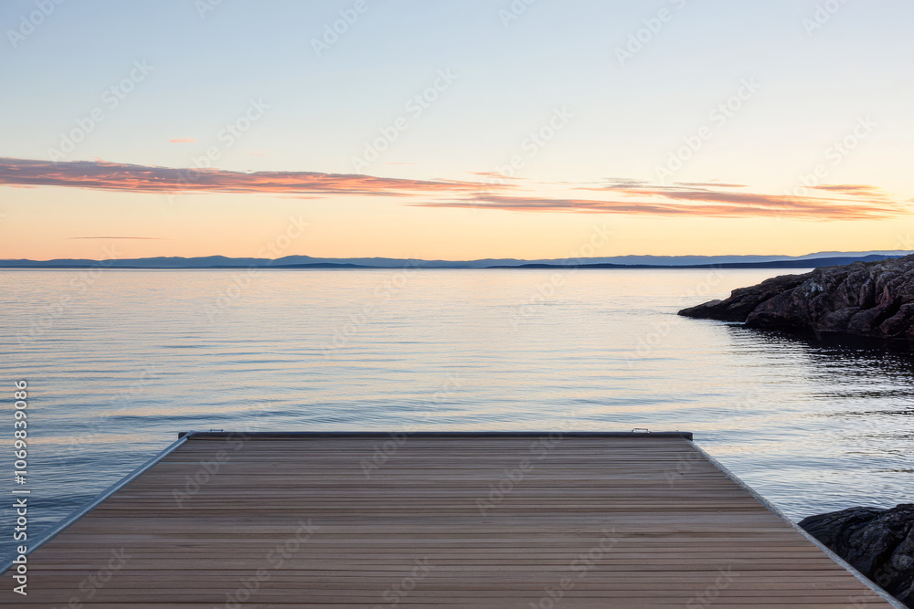 Obraz premium Tranquil wooden dock extending into calm waters at sunset in a coastal landscape