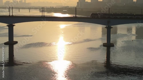 A subway train crossing Dangsan Bridge in Seoul against a backdrop of a reddish-yellow sunrise