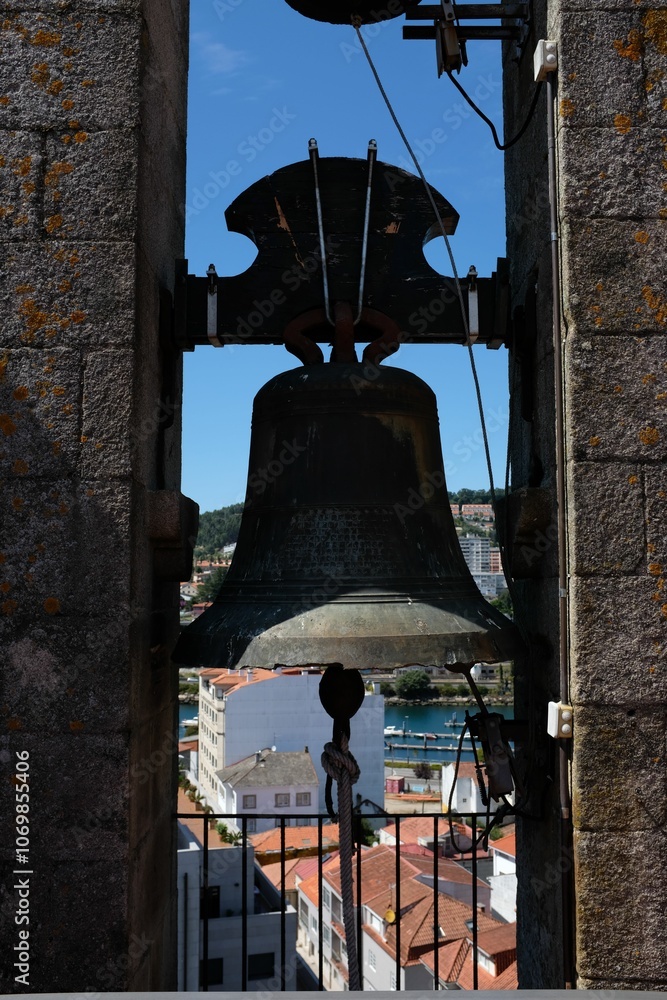 Obraz premium Bronze bell in a stone tower with town view.