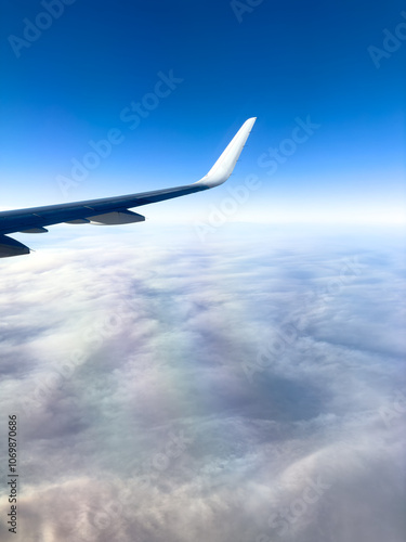 Airplane wing above think clouds below bright blue sky