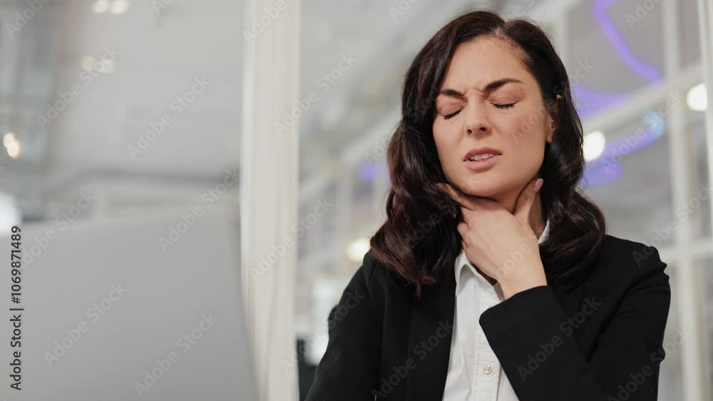 Businesswoman feeling a sore throat at work. She is suffering from an illness, tonsillitis or some other sickness. She is dressed in a white shirt and black jacket. Businesswoman feeling a sore throat at work. She is suffering from an illness, tonsillitis or some other sickness. She is dressed in a white shirt and black jacket.
