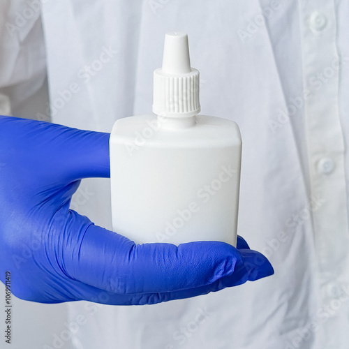 Doctor in white coat and blue medical gloves holds small white bottle of hydrogen peroxide in his hand. Medicine for wound treatment.