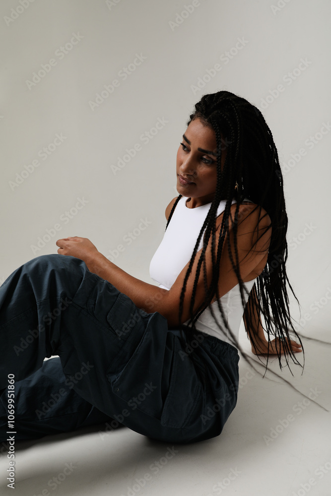 Naklejka premium Young and pretty woman with long dark braids sitting and posing indoor. Vertical.