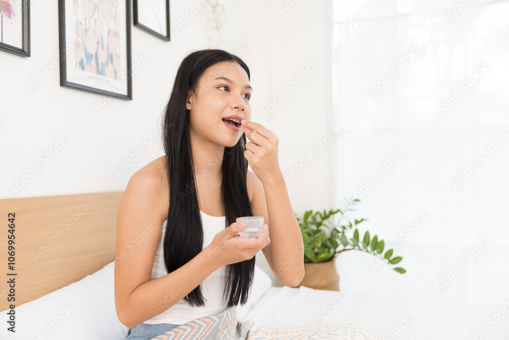 Young Asian woman taking pill while sitting on bed in the bedroom at home. Asian woman stressed and sick Young Asian woman taking pill while sitting on bed in the bedroom at home. Asian woman stressed and sick