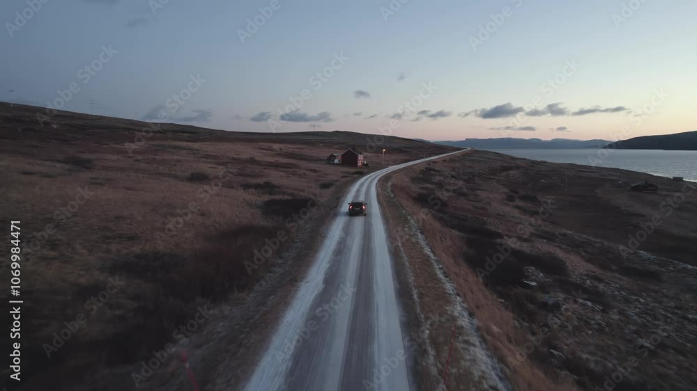A dark SUV drives down a dirt road, on the left side of the road are two small red houses, Norway. A dark SUV drives down a dirt road, on the left side of the road are two small red houses, Norway.