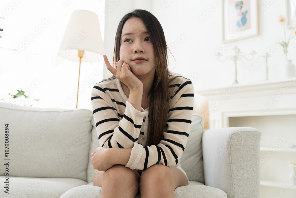 Happy young Asian woman sitting alone on sofa at home Happy young Asian woman sitting alone on sofa at home