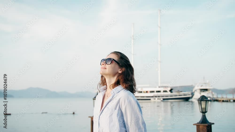 A young Caucasian woman relaxes and enjoys a beautiful view of the sea while standing on the pier A young Caucasian woman relaxes and enjoys a beautiful view of the sea while standing on the pier