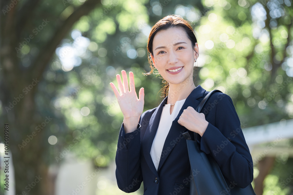 逆光の新緑や緑の背景でビジネススーツを着たカメラ目線の笑顔の美人な女性 営業マンなどのイメージ 手を振る 逆光の新緑や緑の背景でビジネススーツを着たカメラ目線の笑顔の美人な女性 営業マンなどのイメージ 手を振る
