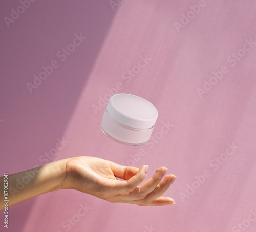 hand holding a  jar of cream on a pink background