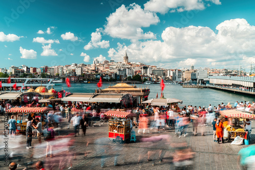 Fototapeta Naklejka Na Ścianę i Meble -  Eminonu, Istanbul. People walking on Eminonu beach. Galata Tower, fish and bread boats in the background. A crowded crowd on a cloudy day. Istanbul, Turkey.