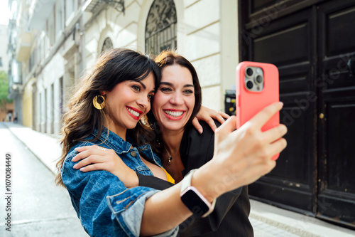 Two pretty friends taking a selfie on the street