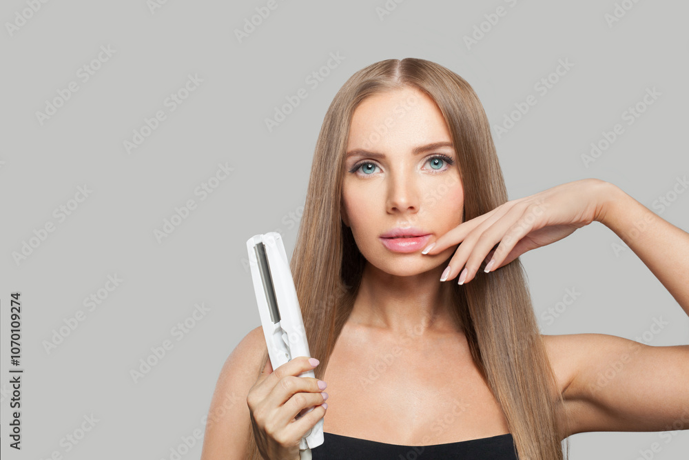 Good-looking brunette woman holding straight hair iron and straightening her long smooth shiny hair on white background. Haircare, hairstyle, hairdressing and hair styling concept Good-looking brunette woman holding straight hair iron and straightening her long smooth shiny hair on white background. Haircare, hairstyle, hairdressing and hair styling concept