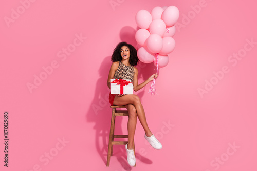 Full size photo of young girl sit chair gift air balloons look empty space gift wear leopard print outfit isolated on pink background